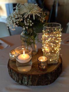 candles are lit on a wooden table with flowers in a vase and glass jars filled with water