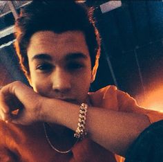 a young man with his hand on his chin looking at the camera while wearing a bracelet