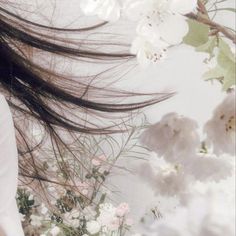 a woman with long hair standing in front of white flowers and greenery on the wall