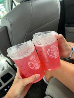 two people holding up pink drinks in the back seat of a car