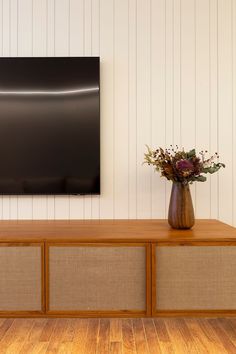 a vase filled with flowers sitting on top of a wooden table next to a wall mounted tv