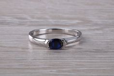 a white gold ring with a blue stone in the center on a wooden table top