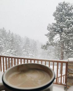 a cup of coffee sitting on top of a table in front of a snow covered forest