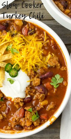 two white bowls filled with chili, cheese and tortilla chips on top of a wooden table