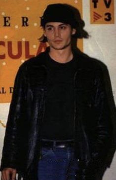 a young man standing in front of a sign and wearing a black hat with his hands in his pockets