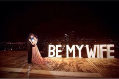 a couple standing in front of the words be my wife