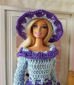 a doll is wearing a crocheted dress and hat with purple trimmings