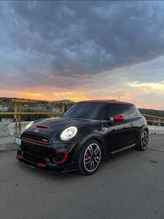 a small black car parked on top of a parking lot next to a bridge at sunset