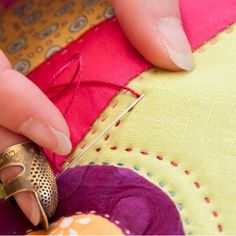 a woman is using a sewing needle to sew on a colorful piece of fabric