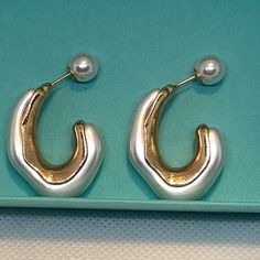 two pairs of gold and silver earrings with pearls on them sitting on a blue surface