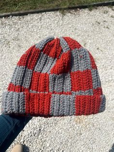 a person wearing a red and gray knitted beanie on their left hand while standing in the street