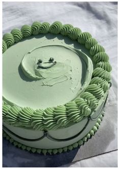 a cake with green icing and a smiling face on it's top is sitting in the snow