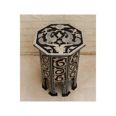 an ornate black and white side table with intricate designs on the top, in front of a beige brick wall