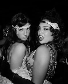 two young women dressed in costume posing for a photo together at a party, one wearing a headband and the other with beads on her hair