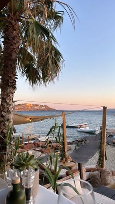 an outdoor dining area overlooking the ocean with boats in the water and palm trees on either side