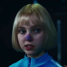 a close up of a person with blonde hair and blue shirt in a dark room