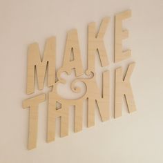 the words make and think are cut out of plywood paper on a white wall