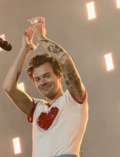 a man with tattoos holding his hands up in the air while standing on stage at a concert