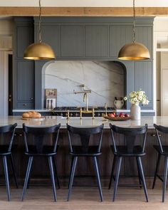 a kitchen with marble counter tops and gold pendant lights hanging over the island, surrounded by black chairs