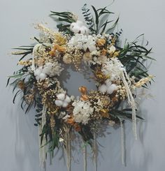 a wreath with white flowers and greenery hanging on the wall next to a gray wall