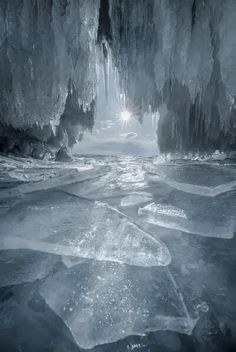 an ice cave with the sun shining through it and frozen water in the foreground