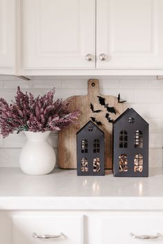 two black houses are sitting on the kitchen counter next to a vase with purple flowers