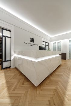 a white marble reception desk in an empty room with wood flooring and large windows