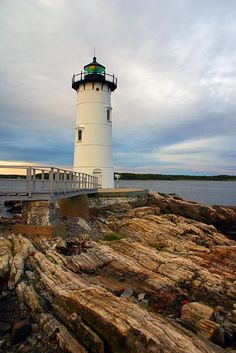 a light house sitting on top of a rock covered shore next to the ocean under a cloudy sky