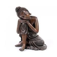 a buddha statue sitting on the ground with his hands clasped to his chest and eyes closed