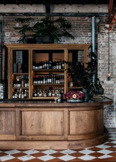 a bar with lots of bottles on top of it next to a brick wall and potted plants