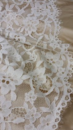 an image of white lace with flowers on the bottom and beige satin material behind it