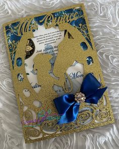 a blue and gold wedding card with a bow on it's side, sitting on white fabric