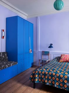 a bed room with a neatly made bed next to a blue cabinet and lamp on the wall