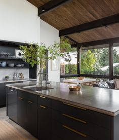 a kitchen with black cabinets and counter tops next to a large open window that looks out onto the backyard