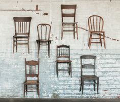 several chairs are lined up against a white brick wall and one chair is missing the seat