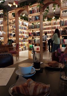 there is a coffee cup and croissants on the table in front of bookshelves