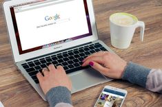 a person typing on a laptop computer next to a cup of coffee and cell phone