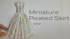 the miniature dress is made from paper and has flowers on it, as well as a hand