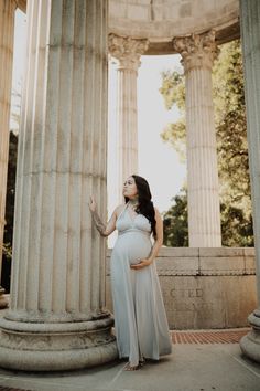 a pregnant woman standing in front of pillars with her hand on her belly and looking up at the sky