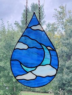 a stained glass window hanging in front of a tree with clouds and water on it