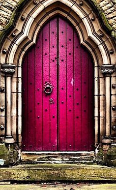 a red door is in front of an old stone building with arched doorway and window