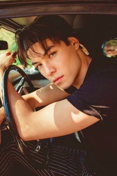 a young man sitting in the driver's seat of a car with his hand on the steering wheel