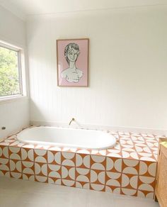 an orange and white bathtub in a bathroom next to a painting on the wall