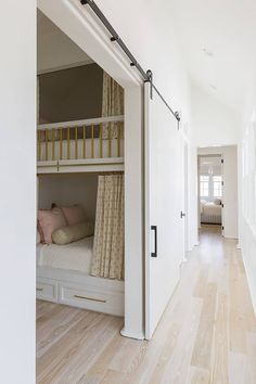 there is a bunk bed in the middle of this hallway with white walls and wood floors