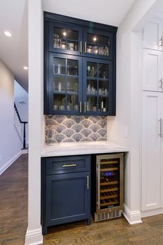 a wine cellar in the corner of a kitchen with dark blue cabinets and white counter tops