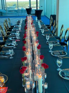 a long table is set with candles and roses in glass vases on the tables