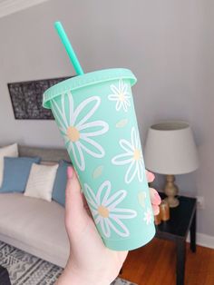 a person holding up a cup with a straw in it and flowers on the side