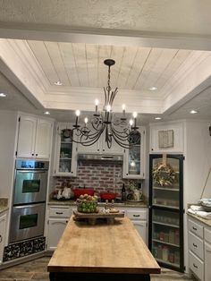 a kitchen with a wooden table in the center and white cabinets on both sides, lights hanging from the ceiling