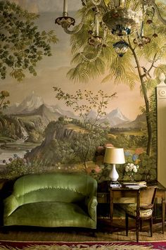 a green couch sitting under a chandelier next to a painting on the wall