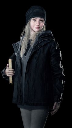 a woman in black jacket and hat holding a skateboard against a dark background with no one around her